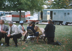 Actors, including Estelle Evans (Sarah Winger), obscured by actor Malcolm Attebury (Silas Newhall) and Don Dubbins (Harley Davis), far left, seated in front of production vehicles.