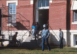 Director Gordon Parks walking down the steps of the courthouse building used for the trial scene with crew members milling about outside.